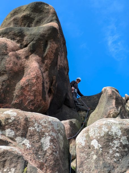 Climber scaling a rocky formation under a clear blue sky.