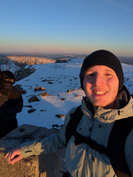 A person smiling in a snowy landscape with mountains under a clear sky.
