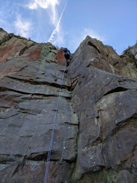 A climber scaling a steep rock face under a clear blue sky.